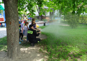 dzieci razem z panem strażakiem leją wodę z węża gaśniczego
